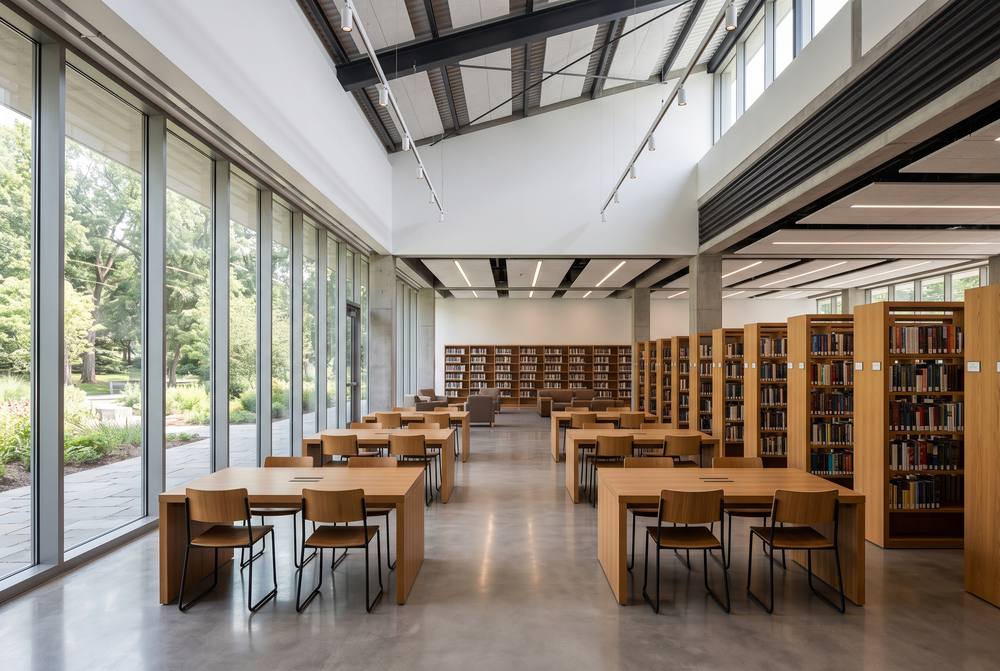A bright, empty library reading room with tall windows and wooden tables